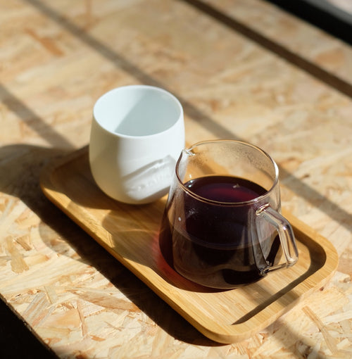 White ceramic cup and glass mug with dark liquid on a wooden tray