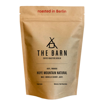 A standing pouch of coffee beans labeled 'THE BARN COFFEE ROASTERS BERLIN HUYE, RWANDA HUYE MOUNTAIN NATURAL', indicating it is a natural process espresso coffee roasted in Berlin.