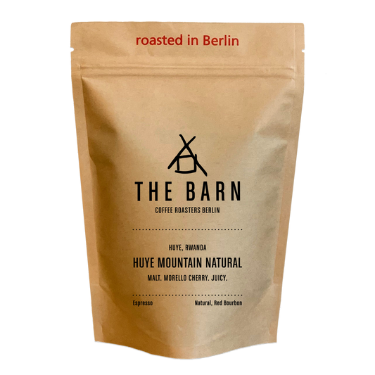 A standing pouch of coffee beans labeled 'THE BARN COFFEE ROASTERS BERLIN HUYE, RWANDA HUYE MOUNTAIN NATURAL', indicating it is a natural process espresso coffee roasted in Berlin.